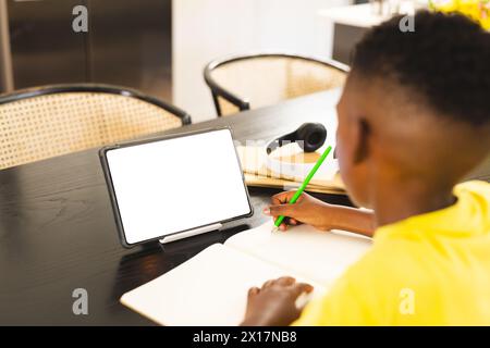 African American boy writing in notebook at home, tablet with blank screen nearby with copy space Stock Photo