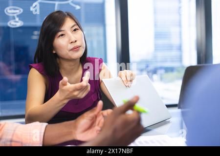 Asian woman discussing with colleague, both using laptops in a modern business office Stock Photo
