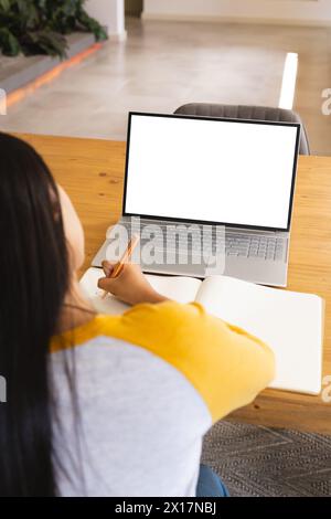 A biracial young female is using a laptop and taking notes with copy space at home Stock Photo