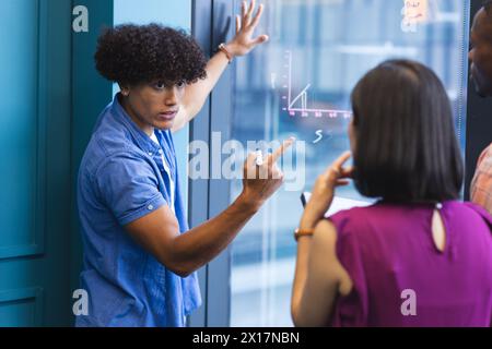 A diverse group of young adults discussing in front of a glass wall in a modern business office Stock Photo