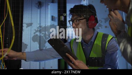Spinning globe and world map against diverse male and female engineers working in server room Stock Photo