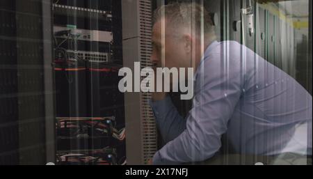 Caucasian senior male engineer talking on smartphone while working in computer server room Stock Photo