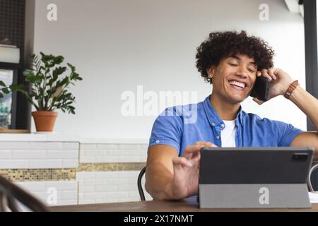 A young biracial man wearing a blue shirt is talking on the phone in a modern business office Stock Photo