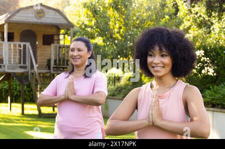Mature biracial woman and young biracial woman doing yoga in garden at home Stock Photo