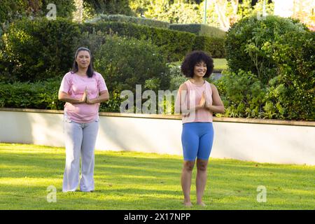 Mature biracial mother and adult daughter practicing yoga in garden at home Stock Photo