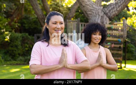 Mature biracial woman and young biracial woman practicing yoga in garden at home Stock Photo