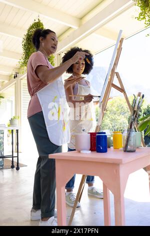 Mother and Daughter, mature biracial woman painting with young biracial woman outdoors at home Stock Photo