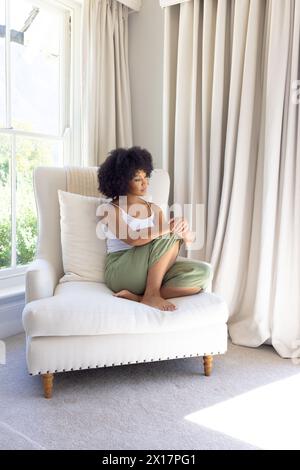 Biracial young woman sitting alone at home, looking thoughtful Stock Photo