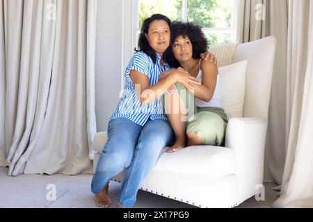 Mature biracial woman hugging young adult daughter, both sitting at home Stock Photo