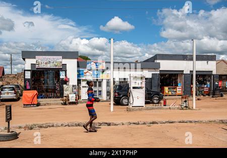 A Ugandan woman, adorned in a vibrant and colorful dress, gracefully walks along a roadside near a gas station, embodying the rich cultural tapestry o Stock Photo