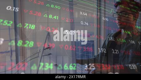 Image of graph and trading board over tired biracial man working over laptop in office Stock Photo