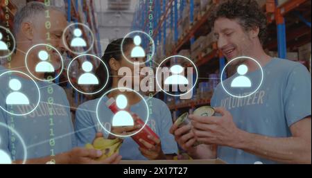 Image of network of icons with binary coding over diverse volunteers in warehouse Stock Photo