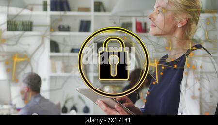 Image of security padlock icon against caucasian woman using digital tablet at office Stock Photo