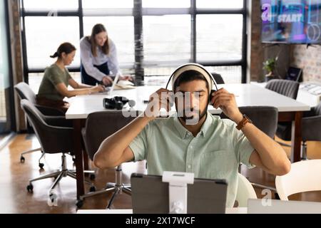 A diverse team works in a modern business office, with a young Asian male focusing on a computer Stock Photo
