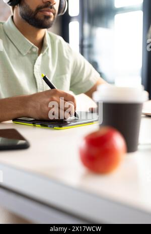 Asian male wearing headphones writing on digital tablet in a modern business office Stock Photo