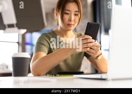Middle-aged Asian woman checking smartphone at work in a modern business office Stock Photo