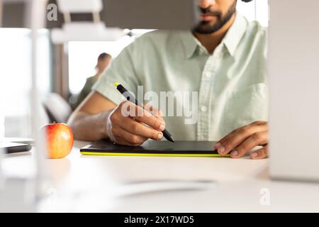 Asian male professional drawing on digital tablet in a modern business office, wearing a green shirt Stock Photo