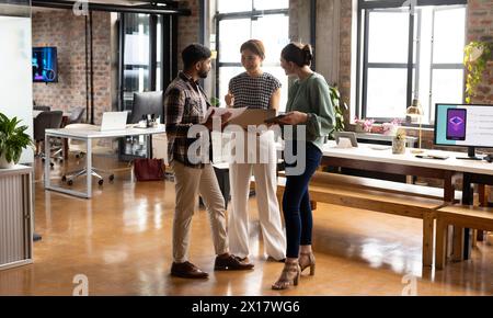 Diverse team discussing project in modern business office, mature Asian woman guiding Stock Photo