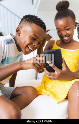 African American brother laughing with sister, both looking at smartphone at home Stock Photo