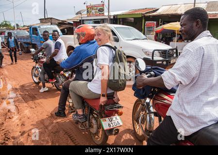 Women passenger on motorcycle navigates muddy Entebbe streets in Uganda with fellow riders.She seems very happy about the exciting motorcycle ride Stock Photo