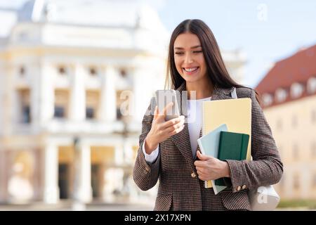 Smiling student using smartphone standing outdoors at university campus Stock Photo