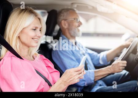 Smiling senior woman using phone, man drives in car Stock Photo