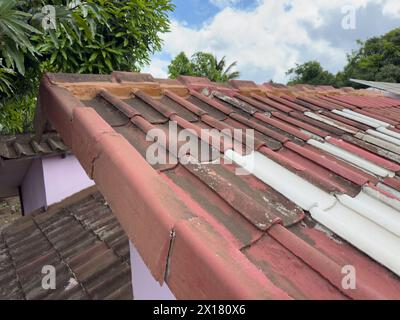 Damaged tiled house roof on blue sky background Stock Photo