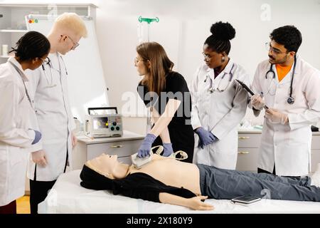 A woman lying on a bed while a group of doctors stand around her, discussing her medical condition and treatment options. Stock Photo