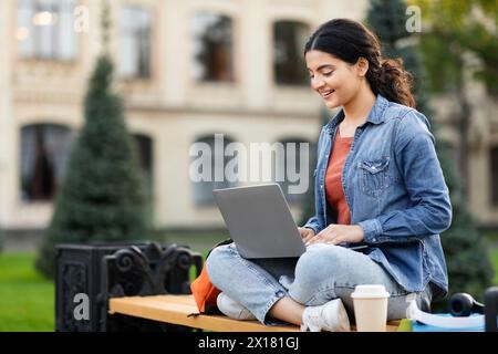Focused woman student working on laptop outside Stock Photo