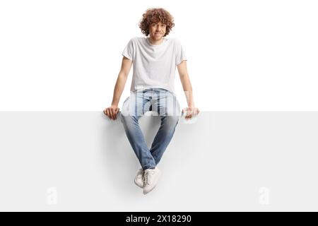 Cute guy with curly hair sitting on a blank panel isolated on white background Stock Photo