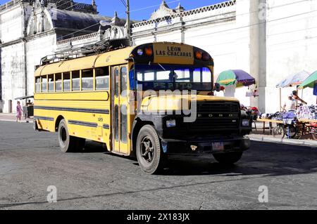Leon Nicaragua, Yellow school bus drives on a street past historic buildings and market stalls, Nicaragua, Central America, Central America Stock Photo