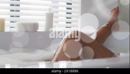 Image of light spots over african american woman taking bath Stock Photo