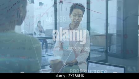 Two businesswomen are shown working together in an office, enjoying coffee and chatting one woman is Stock Photo