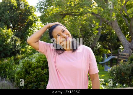 Mature biracial woman standing outside, stretching neck and smiling at home Stock Photo