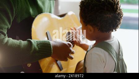 Image of light flashing over african american father and son playing guitar Stock Photo