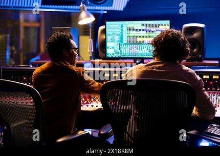 Professional sound engineer and artist working together on a new track, using digital audio software to edit and process tunes. Experts team collaborating on music, mixing at control room board. Stock Photo