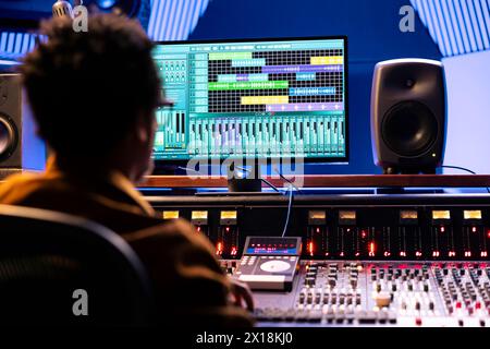 African american tracking engineer working with editing software on pc, producing new music for his album. Sound designer adjusting recordings setting and volume levels at control room panel board. Stock Photo