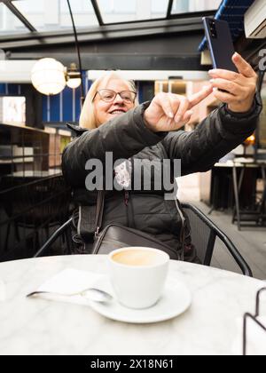 pov senior woman laughing enjoying taking selfie with the cell phone with the coffees already finished Stock Photo