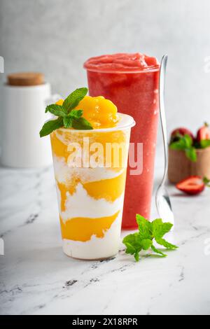 Mango smoothie with whipped coconut cream swirled in a tall cup and strawberry watermelon smoothie Stock Photo