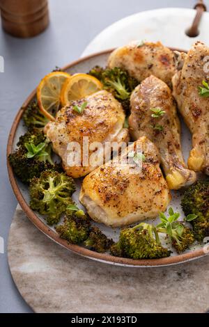 Chicken drumsticks and thighs with broccoli roasted on a serving plate for dinner or lunch with garlic and herbs Stock Photo