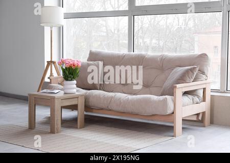 Stylish interior of living room with beige sofa, lamp and tulips on coffee table Stock Photo