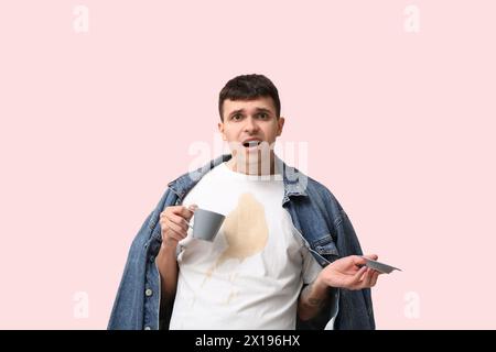 Stressed young man with coffee stains on his t-shirt on pink background Stock Photo