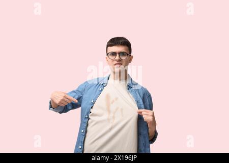 Stressed young man with coffee stains on his t-shirt on pink background Stock Photo