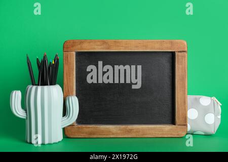 Pencil holder with pencils and blackboard on green background Stock Photo