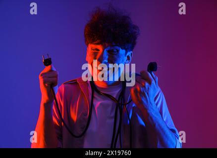 Electrocuted young man with burnt face and plugs on dark background, closeup Stock Photo