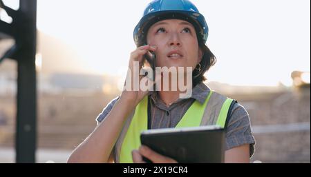 Asian woman, phone call and tablet, construction worker and inspection of building site for project management. Architecture, engineer and Stock Photo
