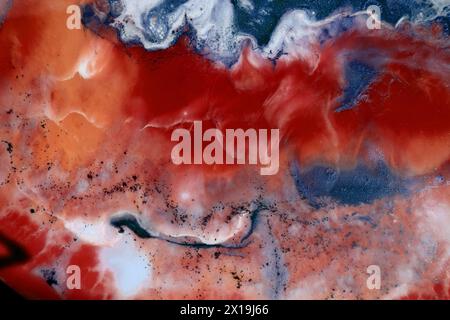 Abstract marble background of red, blue and white colors. Chaotic spots, colors mix with each other. Black dots. The background resembles water waves. Stock Photo