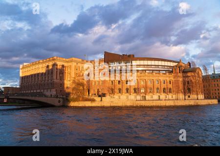 The swedish parliament building in Stockholm at sunset, orange tones, cloudy sky, the river Norrström in the foreground. Stock Photo