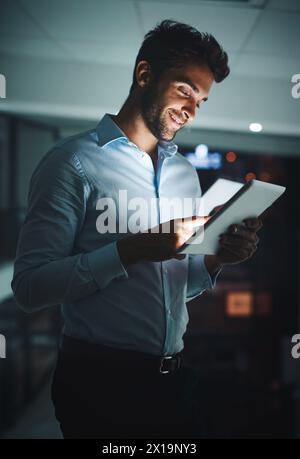 Happy, businessman and night with tablet for research, networking or tech support at office. Young man, employee or IT specialist working late on Stock Photo