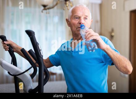 Senior man using elliptical trainer and drinking water Stock Photo